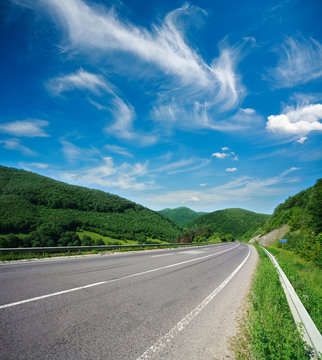 Asphalt road in summer green forest mountains on blue sky background