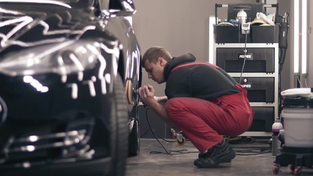 Polishing car with polish mashine. Worker in red suit cleaning a black expensive car.