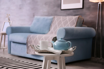 Stylish table with tea set near cozy sofa in living room interior