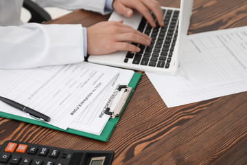 Male doctor with laptop at table in office. Health insurance concept