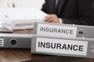 Folders with documents and man working on background. Insurance concept
