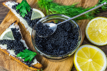 Black caviar on a sandwich. Put a silver spoon on the sandwich. - obrazy, fototapety, plakaty