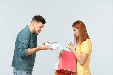 Angry man scolding his wife who has spent a lot of money for shopping, against light background