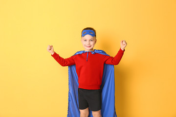 Cute boy in superhero costume on color background