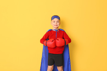 Cute boy in superhero costume on color background