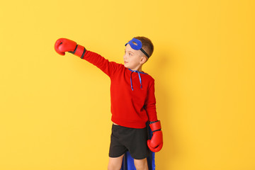 Cute boy in superhero costume on color background