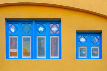 Blue old style wooden windows, symmetry in open doors, yellow house wall background in small town, minimal style of simplicity, trendy look, contrast bright colors, modern postcard art design concept