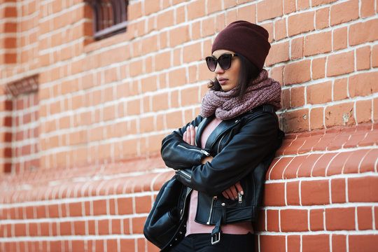 Young fashion woman in black leather jacket leaning on brick wall