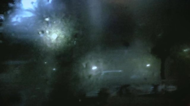 Blurred view of the street and street lights from a condensed bus window after rainfall.