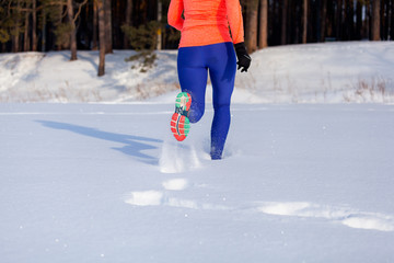 Close-up of a young woman in bright purple leggings and sneakers running through the winter snow on a bright winter day, rear view. Following from a sneaker in the snow