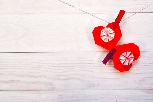 valentine day concept. origami paper hearts hanging on a rope on a clip on white rustic background