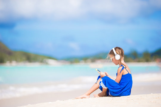 Little girl listening the music by headphones on the beach