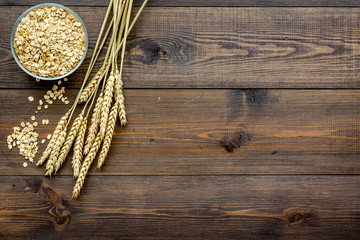 Obraz premium Cereals concept. Oatmeal in bowl near sprigs of wheat on dark wooden background top view copy space