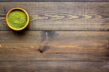 Powdered matcha green tea in bowl on dark wooden background top view copy space