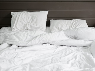 white bedding sheets and pillow on natural stone wall room background ,Unmade messy bed after comfort sleep concept