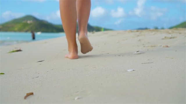Close up female feet walking barefoot on sea shore at sunset. Slow Motion.