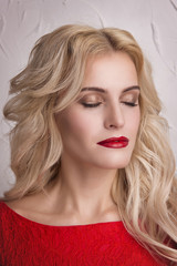 Evening makeup on blonde in red with long curled hair close-up on gray background.