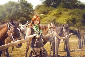 Redhead girl in casual clothes on the background tied the horses on a summer day