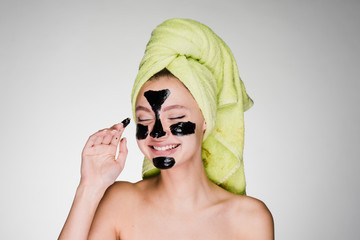 happy woman with a towel on her head applied a mask to problem areas of the skin