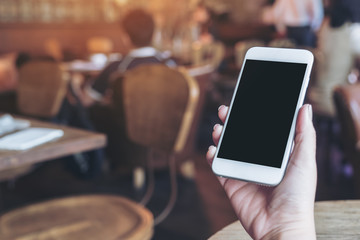 Mockup image of woman's hands holding mobile phone with blank black desktop screen in cafe