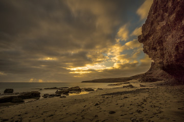 Fototapeta na wymiar Beach on a Canarian island with dark clouds and big lava mountains at sunset