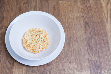 Uncooked Instant Noodles in white bowl and Plate on wooden table