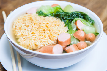 Instant Noodles with sausage with Pak Choy or Chinese Cabbage in white bowl and Plate on wooden table