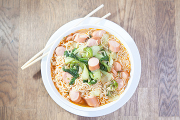 Instant Noodles with sausage with Pak Choy or Chinese Cabbage in white bowl and Plate on wooden table