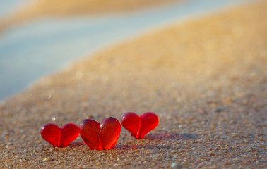 Fototapeta premium Three red glass heart lay on sand. Inner glow of light. Valentine day post card