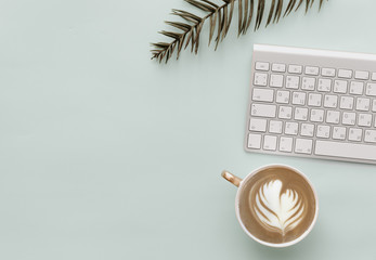 Minimalist Flat Lay Hipster Desktop With keyboard, coffee and green tropical leaves