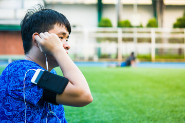 Asian sport man is listening his favorite song by smart pohne that hold on his arm during relax in sport ground.