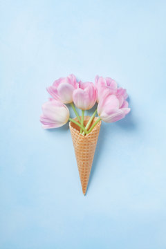 Waffle cone with pink tulips bouquet on pastel blue background top view. Flat lay..