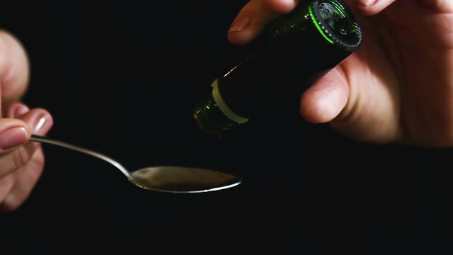 man dripping cough syrup on tablespoon. Liquid medicine flows out green bottle