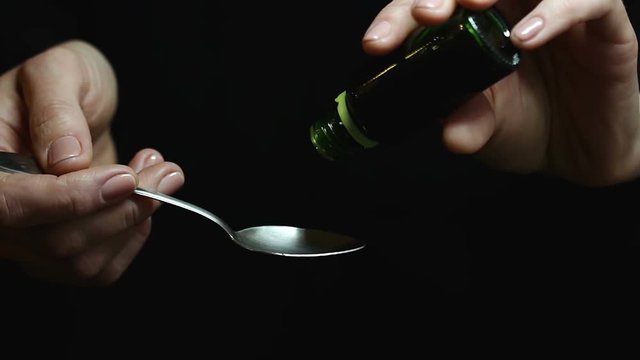 Woman drips liquid medicine out of green bottle into spoon. Few drops of syrup