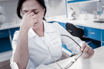Need to take a break. Poor female scientist wearing a lab coat taking off her glasses and pressing...
