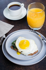 Rye bread toasts with fried spinach and egg with cup of coffee and orange juice on blue table background. Healthy Breakfast Food Concept. Copy Space