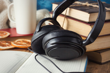 Books are stacked, Headphones, White Cup, Orange Slices, open Diary on a wooden background. The Concept of Audio Books and Audio Education