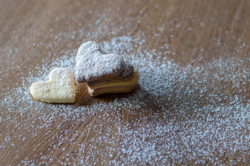 Close-up of cookies in the shape of a heart lying on the wooden table with sugar powder background