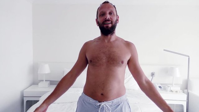 Happy man falling on bed at home, super slow motion
