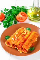 Traditional Italian pasta cannelloni. Baked tubes stuffed with minced meat with parmesan cheese and bechamel sauce on a white wooden table.