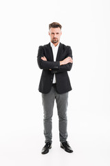 Full-length portrait of handsome businessman in suit posing on camera with brooding look and hands crossed, isolated over white background