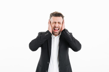 Photo of businessman in suit with closed eyes screaming and covering his ears with both hands, isolated over white background