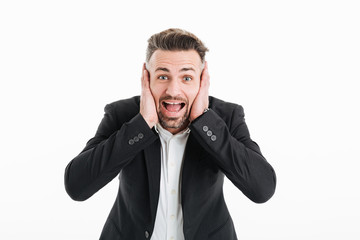 Photo of excited businesslike man in suit yelling on camera and covering his ears with both hands, isolated over white background
