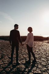 Fototapeta premium Young loving couple of teenagers in sunglasses holding hands on the lake shore.