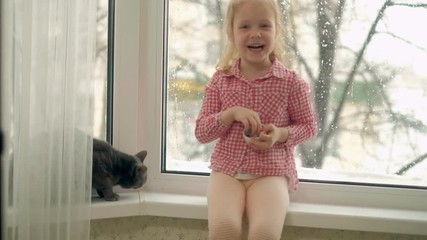 a little girl is feeding a cat sitting by the window