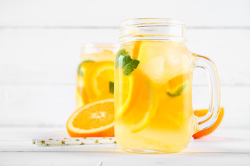 Orange detox water in mason jars on a white wooden table. Healthy food, drinks.