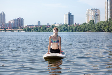 Young beautiful woman meditating on a river at SUP paddleboarding 