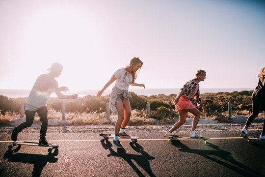 Group of hipster friends longboarding on the road in summer