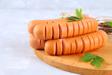 Fried chopped sausages on a wooden board on a gray concrete table.