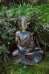 traditional small smiling buddha monk statue on ground in a garden